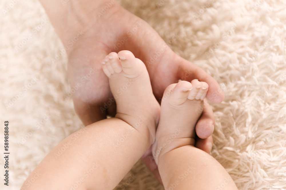 Small naked baby legs in mom's hands