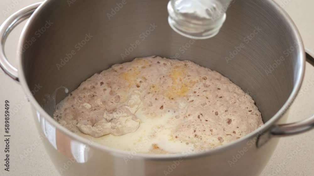 Pouring fresh milk into a metal bowl containing wheat flour, eggs and yeast starter - preparation of dough Pouring fresh milk into a metal bowl containing wheat flour, eggs and yeast starter - preparation of dough