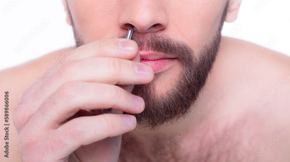 Close up photo of young bearded man removing nose hair with tweezers, isolated over white background