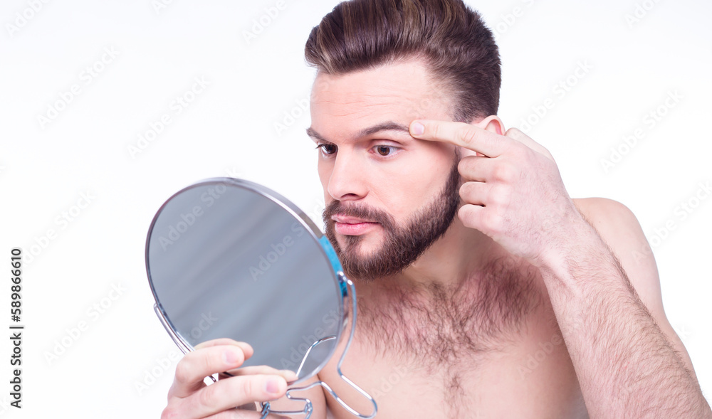 Close up portrait of frustrated, naked bearded man looking in the mirror for acne on his face isolated on white background Close up portrait of frustrated, naked bearded man looking in the mirror for acne on his face isolated on white background