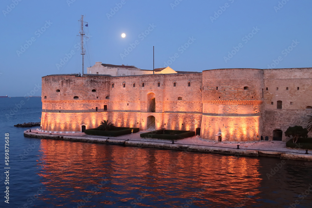 Aragonese Castle of Taranto at the first light of dawn with the full moon in the sky. Puglia, Italy 
