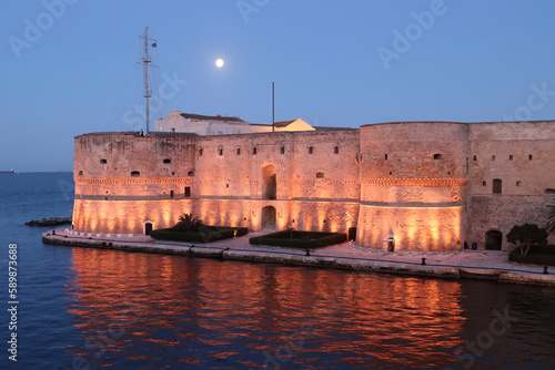 Aragonese Castle of Taranto at the first light of dawn with the full moon in the sky. Puglia, Italy 