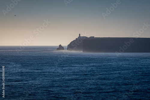 As the sun dips below the horizon, an evening view captures the southwesternmost point of Europe, Cape Cabo de São Vicente, with its saint vincent lighthouse and a solitary seagull flying in the sky. photo