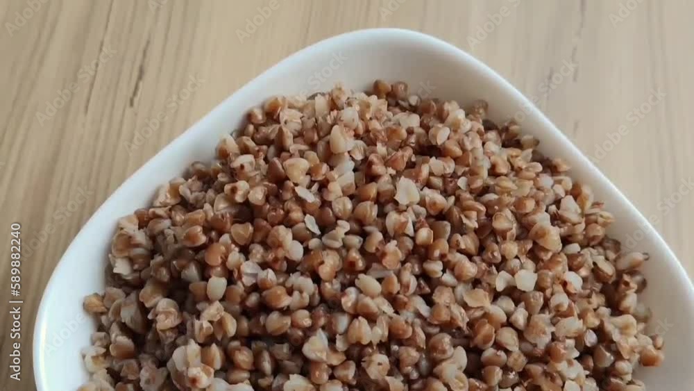Boiled buckwheat porridge in a white ceramic plate on a brown wooden background Boiled buckwheat porridge in a white ceramic plate on a brown wooden background