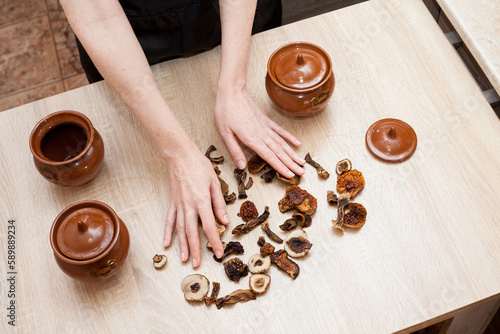 A girl with dried mushrooms on the table, and ceramic vintage brown cooking pots stand in the kitchen. Image for your creative design or interesting illustrations.