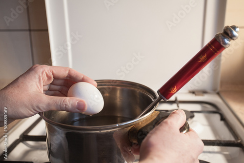 A girl boils egg in a metal pan on a white gas stove in the kitchen. Image for your creative decoration or design.