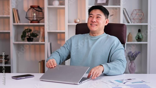 Relaxed Asian satisfied businessman happy man finish computer work close laptop relaxing in sunny warm comfortable office male specialist stretch muscles put hands behind head day end job well done. photo