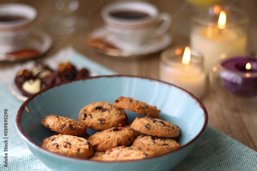 Plate of chocolate pralines, bowl of cookies, cups of tea, glasses of juice and lit candles on the table. Selective focus. Plate of chocolate pralines, bowl of cookies, cups of tea, glasses of juice and lit candles on the table. Selective focus.