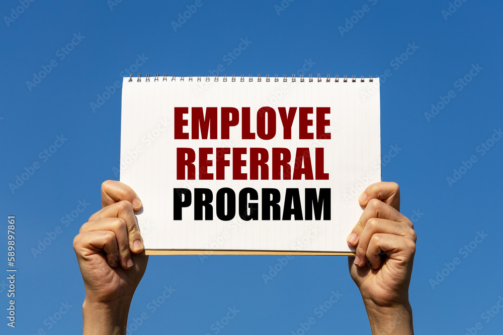 Employee referral program text on notebook paper held by 2 hands with isolated blue sky background. This message can be used as business concept about employee referral program. Employee referral program text on notebook paper held by 2 hands with isolated blue sky background. This message can be used as business concept about employee referral program.