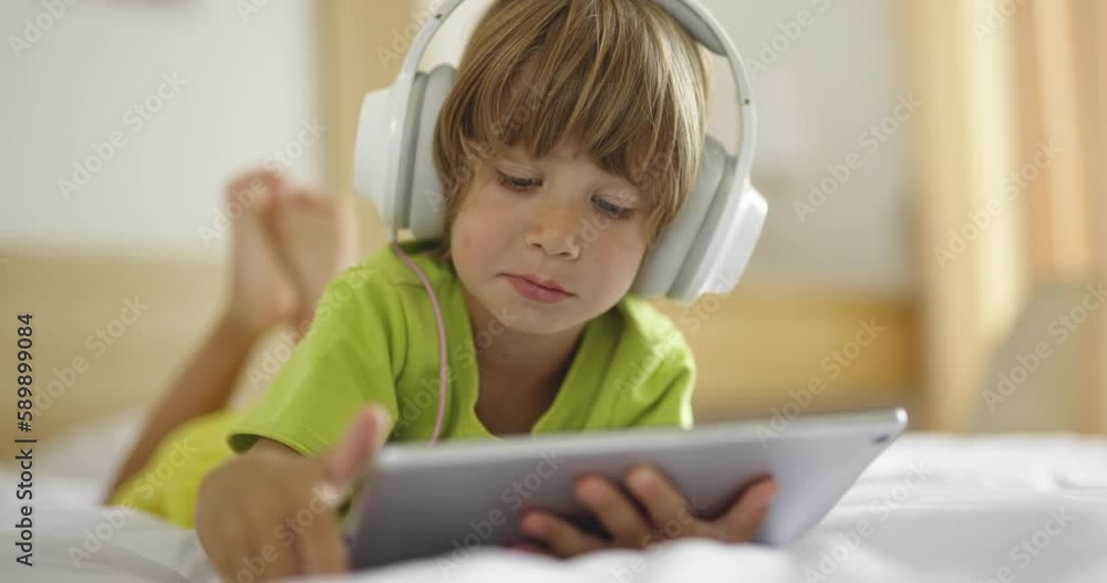 Child spends time with electronic device, tech addiction. Boy in headphones Child spends time with electronic device, tech addiction. Boy in headphones