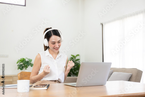 Slika na platnu Pretty Asian girl in headphones listening to music happily on her laptop and mobile