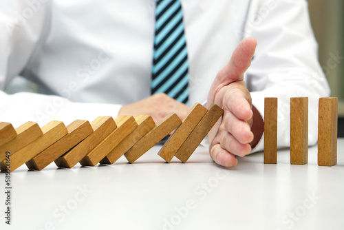 Hand prevent wooden block falling domino effect from continuous fall. Risk management, strategic, insurance and business plan concept.