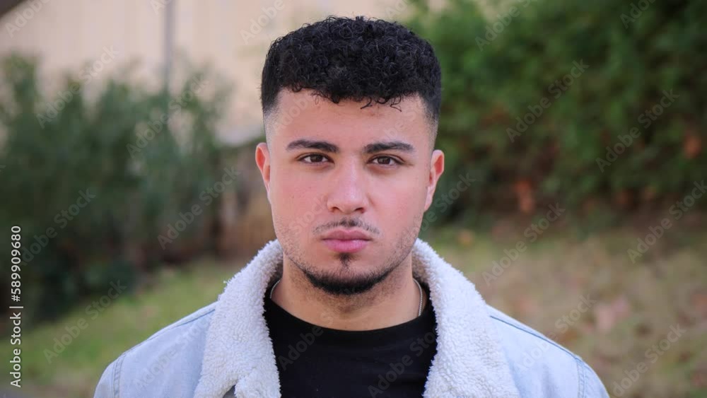 Close up portrait of young guy looking serious at camera standing outdoors. Front view of handsome isolated man with pensive attitude. Head shoot of thoughful teenage student at university campus Close up portrait of young guy looking serious at camera standing outdoors. Front view of handsome isolated man with pensive attitude. Head shoot of thoughful teenage student at university campus