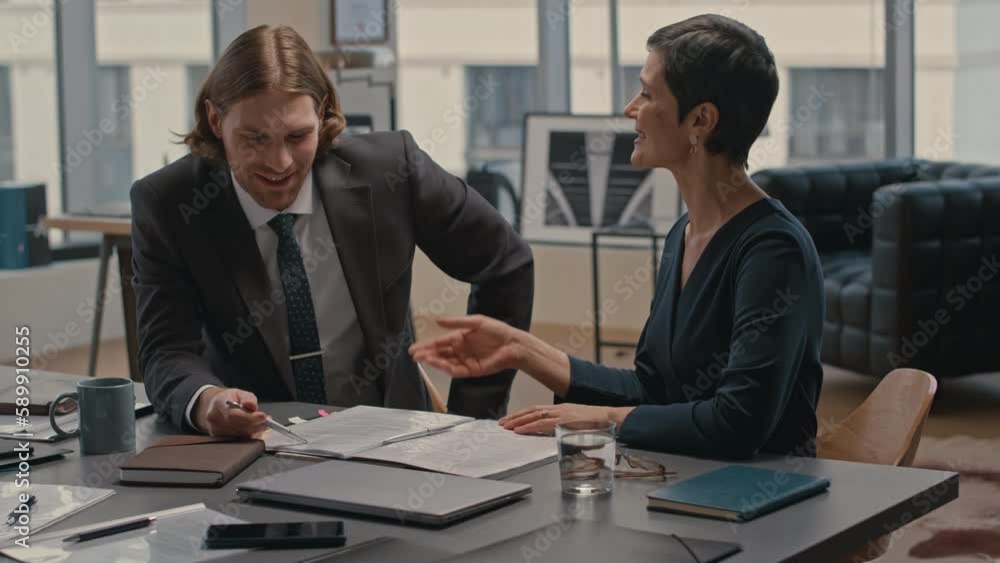 Waist up of young Caucasian businessman consulting with female lawyer about business contract he is about to sign, having meeting in modern office Waist up of young Caucasian businessman consulting with female lawyer about business contract he is about to sign, having meeting in modern office