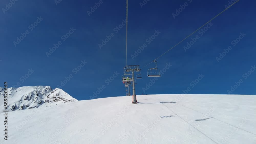 4K video clip of four person ski chair lift in blue sky going up a mountain with skiers on the piste below
4K video clip of four person ski chair lift in blue sky going up a mountain with skiers on the piste below