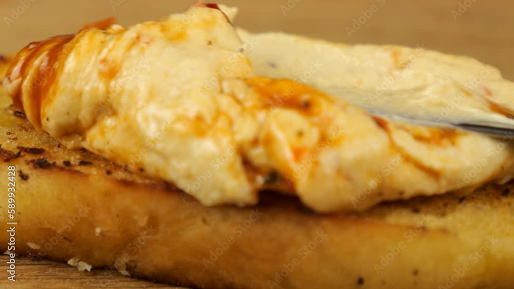 Hummus is spread with a knife on a piece of toasted bread against a background of assorted appetizers. Food for vegans.