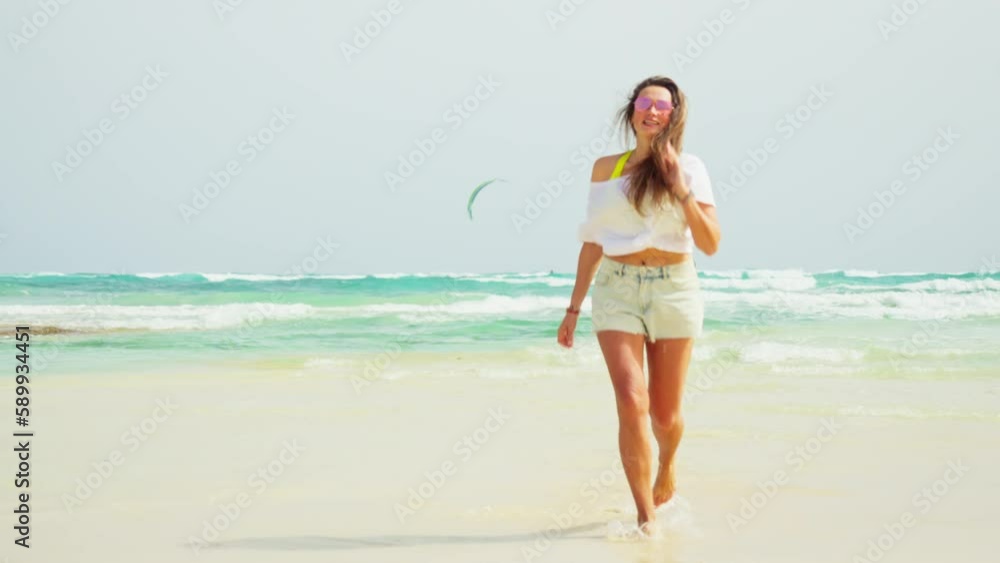 The girl walks along the beach, white sand and blue sea. Kiteboarding.