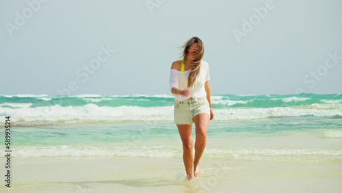 The girl runs along the beach, approaches. White sand and blue sea.