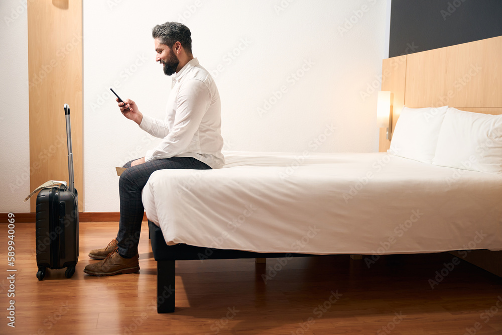 Contented man using mobile phone in hotel room