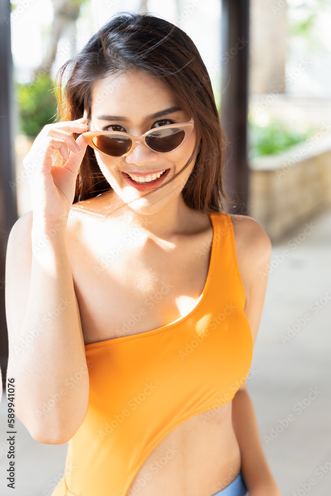 Happy smiling relaxed summer woman looking at you, wearing sunglasses and bikini swimsuit, sunbathing at sunny tropical summer resort and spa environment Happy smiling relaxed summer woman looking at you, wearing sunglasses and bikini swimsuit, sunbathing at sunny tropical summer resort and spa environment