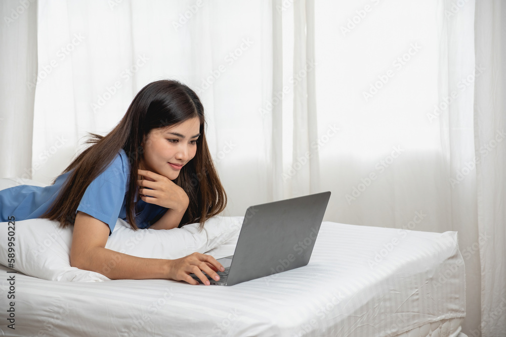 Young Asian woman with beautiful face, long hair, blue shirt lying on bed in white bedroom at home with cup of coffee and video call with laptop talking to relatives on vacation. holiday concept. Young Asian woman with beautiful face, long hair, blue shirt lying on bed in white bedroom at home with cup of coffee and video call with laptop talking to relatives on vacation. holiday concept.