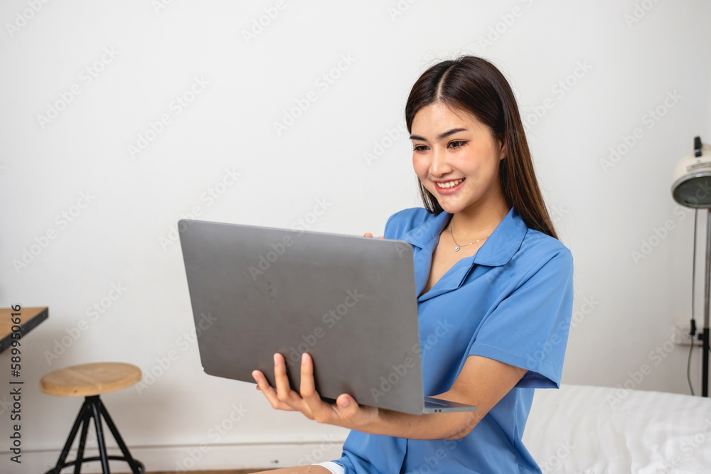 Young Asian woman with beautiful face, long hair in blue shirt sitting on white bedroom bed at home with cup of coffee and video call with laptop talking to relatives on holiday. vacation concept. Young Asian woman with beautiful face, long hair in blue shirt sitting on white bedroom bed at home with cup of coffee and video call with laptop talking to relatives on holiday. vacation concept.