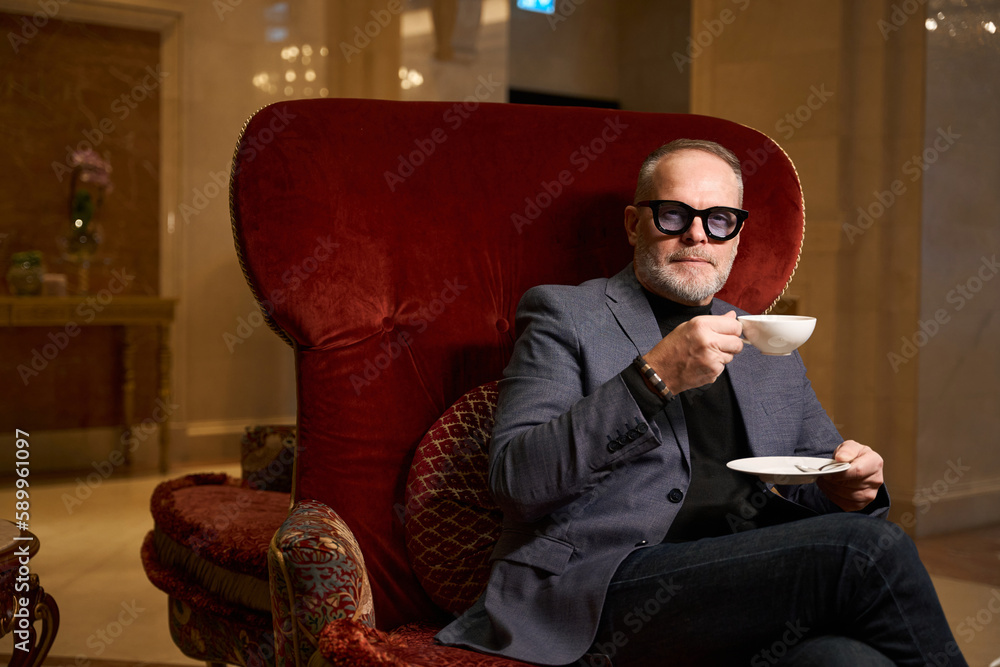Imposing man sits in a luxurious velvet chair Imposing man sits in a luxurious velvet chair