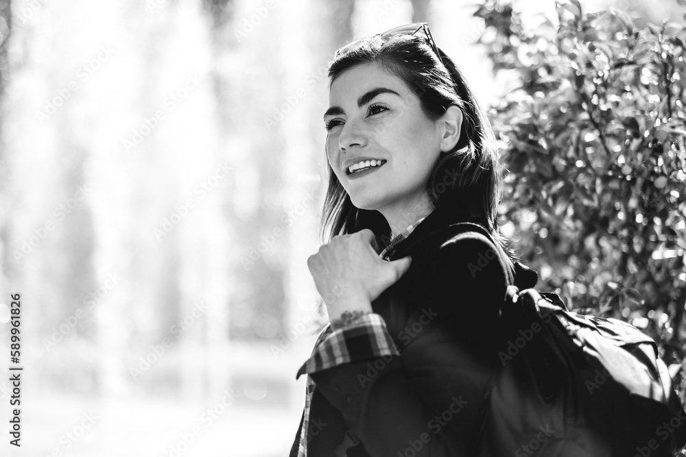 Modern, beautiful and young executive: sophisticated woman with sunglasses and backpack, happy at urban park with water fountain behind (in black and white) Modern, beautiful and young executive: sophisticated woman with sunglasses and backpack, happy at urban park with water fountain behind (in black and white)