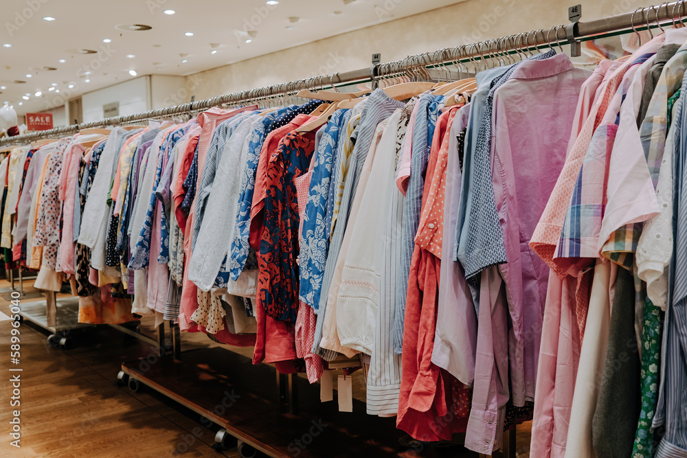 Colorful summer clothes hang on shelf hangers in store. Modern