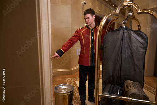 Slika na platnu Young bellboy is pushing a cart with luggage around lobby