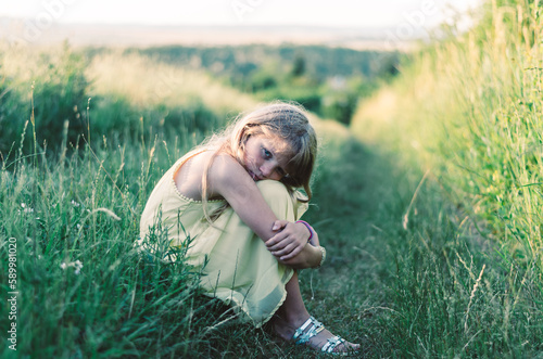 sad child outdoors in countryside sitting in grass