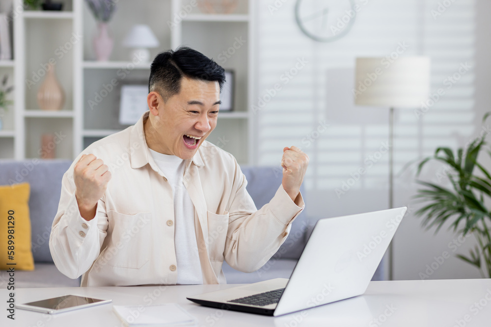 Asian working remotely from home office with laptop, businessman received notification of good achievement results, freelancer satisfied with work rejoices and celebrates victory and triumph.