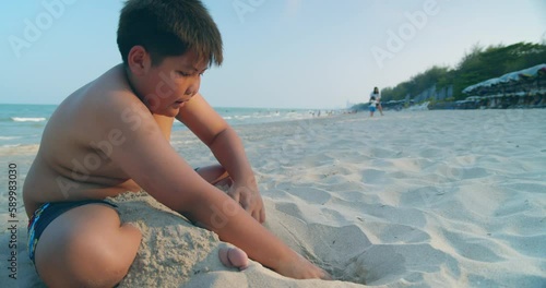 (Slow motion) A happy Asian boy who had a rather chubby figure, enjoying and playing in the sand on the sea beach in the evening sunset time.