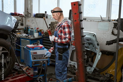 Worker in a plaid shirt stands in car repair shop