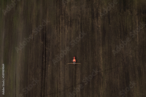 Top view frome drone of a red tractor plows the ground in the field for planting countryside