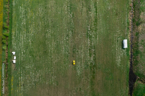 Top view of a yellow retro car on the summer green meadow field with white flowers and coils of hay distant plan
