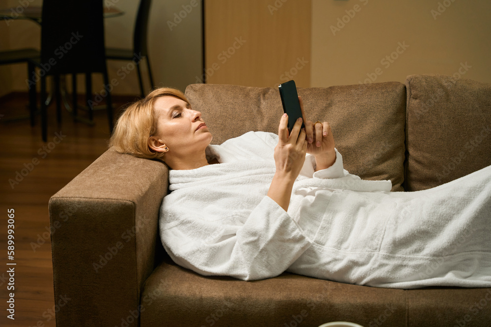 Calm middle-aged lady lies on the sofa in a bathrobe Calm middle-aged lady lies on the sofa in a bathrobe