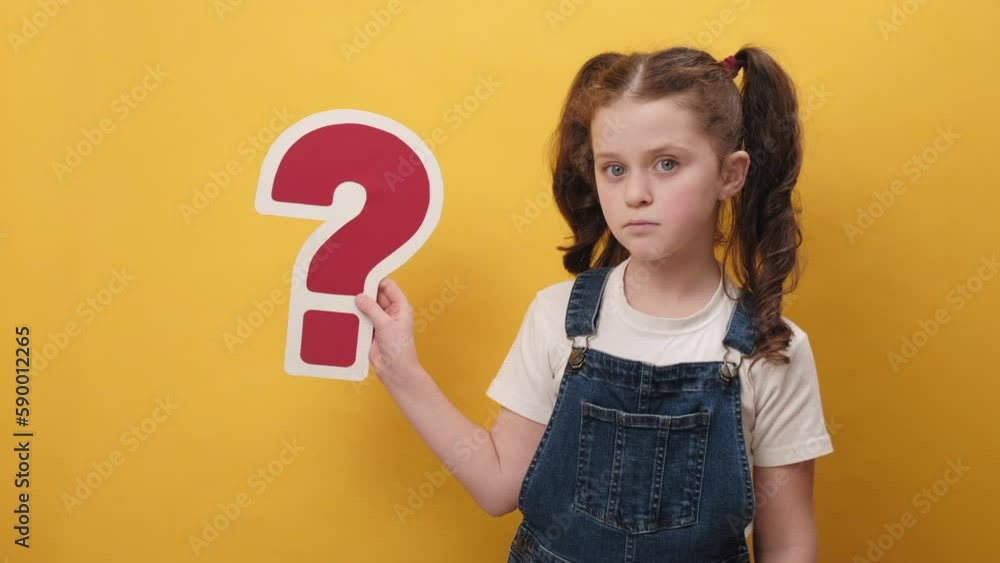 Portrait of thoughtful little girl kid 7-8 old years holding big red question mark sign, posing isolated over yellow color background wall in studio. Childhood lifestyle and confusion concept Portrait of thoughtful little girl kid 7-8 old years holding big red question mark sign, posing isolated over yellow color background wall in studio. Childhood lifestyle and confusion concept