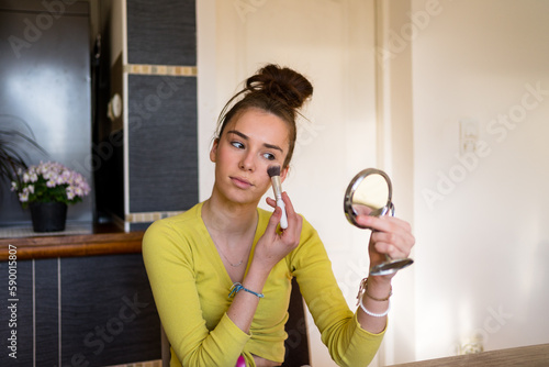 Young teenage woman doing make up in her living room, using her make up brush. 