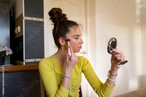 Young teenage woman doing make up in her living room, using her make up brush. 