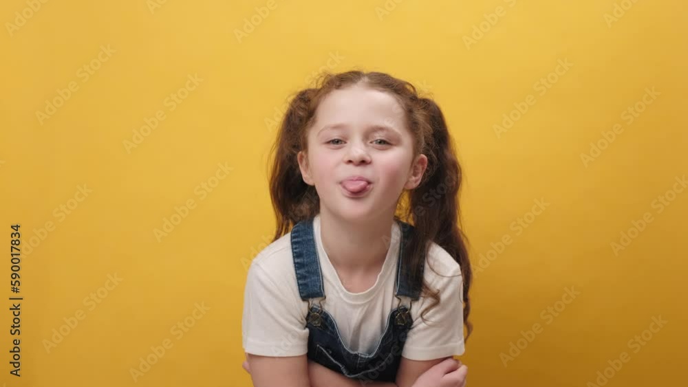 Portrait of funny bully preteen girl kid showing tongue making faces at camera, fooling around, joking, aping with silly face, teasing, posing isolated on yellow color background wall in studio Portrait of funny bully preteen girl kid showing tongue making faces at camera, fooling around, joking, aping with silly face, teasing, posing isolated on yellow color background wall in studio