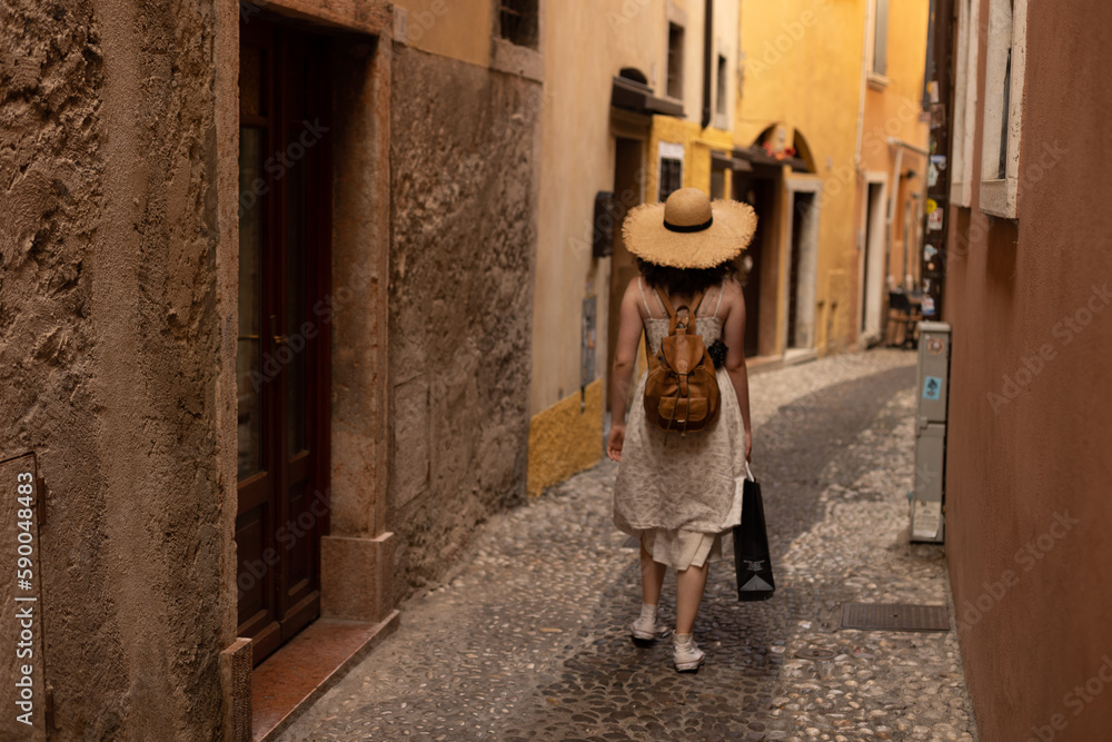 Travelling young teenage girl with a leather bag and a straw hat, exploring the streets of a picturesque town of Lake Garda in Italy Travelling young teenage girl with a leather bag and a straw hat, exploring the streets of a picturesque town of Lake Garda in Italy
