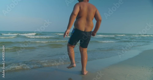 (Slow motion) A happy Asian boy who had a rather chubby figure, running and enjoying in the water on the sea beach in the evening sunset time.