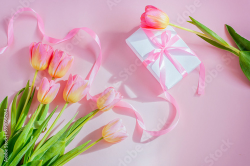 gift tied with a long pink ribbon and tulips on a pink light background. High quality photo