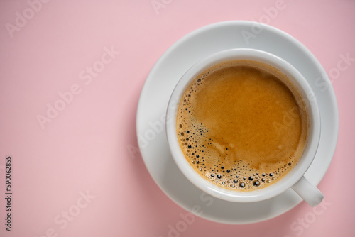 White porcelain coffee cup with saucer over pink background, top view, copy space, closeup. Hot coffee in a breakfast