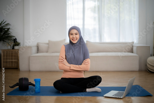 Beautiful muslim girl cross arm at chet smile to camera, prepare to do work out follow by online clip with her equipment and water bottom. photo