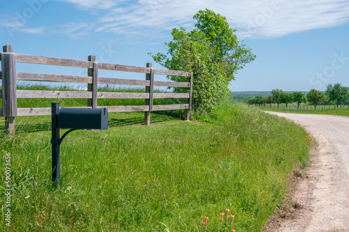 A mailbox and wooden fence on the side of a gravel road.