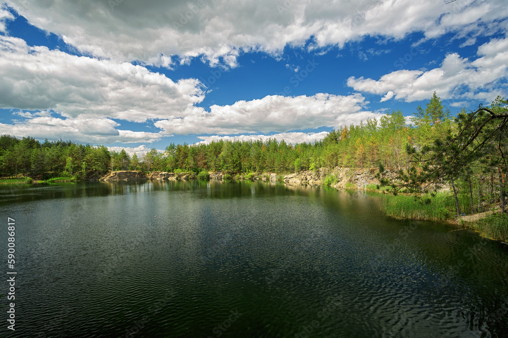 A lake with rocky shores, at the edge of the forest, blue sky with white clouds