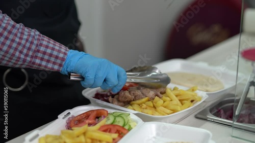 Cook prepares lunch boxes with Greek kalamaki dish with souvlaki meat, fries and vegetables
