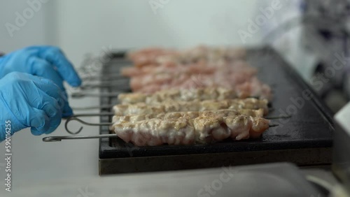 Cook turning pork on skewers on a grill in a commercial kitchen. Male person cooking meat fillet on a hot iron pan in a fast food restaurant